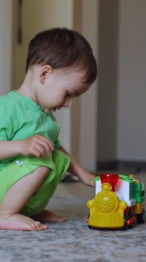Trenle oynayan sağlıklı beyaz bir erkek bebek. Oyuncak araba gider ve çocuk neşeyle onu takip eder. Dikey video