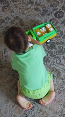 Aktif koyu renk saçlı çocuk halıda sürünüyor. Çocuk oyuncak arabayla oynuyor. Üst Manzara. Dikey video