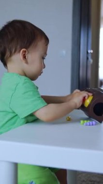 Masada oturan sevimli küçük bir çocuk. Çocuk odada oyuncaklarla oynuyor. Yan görüş. Dikey video