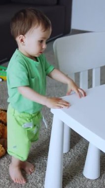 Küçük tatlı çocuk şu anda odasında. Çocuk bir dizi parlak oyuncakla masada oturmak istiyor. Yukarıdan bak. Dikey video