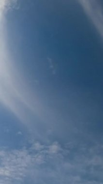 Mavi gökyüzü tarafından ışık bulutları yayılıyor. Güneş yumuşak bulutlarla kaplıdır. Düşük açılı bakış açısı. Dikey video