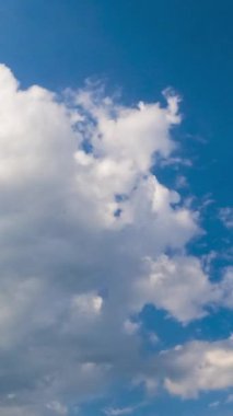 Havada yavaşça süzülen beyaz bulutlar ile şaşırtıcı masmavi gökyüzü. Bulutlar parlak yaz güneşiyle aydınlanıyor. Düşük açılı zaman dilimi. Dikey video