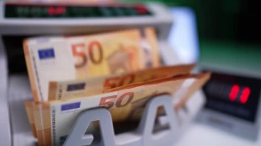 50 avro değerinde turuncu banknotlar ve yeşil banknotlar para sayma makinesine düşüyor. Kapatın. Banka ekipmanları.