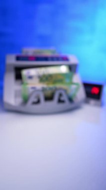 Para, para sayma makinesine konur. 100 avroluk banknotlar ekipmanlardan alınıp masaya konuyor. Kapatın. Arkaplan bulanık. Dikey video.