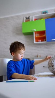 Küçük bebek, odada, masada oturuyor. Beyaz, şirin bir oğlan çocuğu boyama kitabını açıyor. Dikey video.