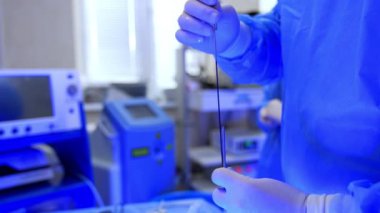 Cüppeli ve lateks eldivenli tanınmayan doktor tıbbi aletleri tutuyor ve ayarlıyor. Cerrah ameliyatta kullanmak için endoskop hazırlıyor. Kapat..