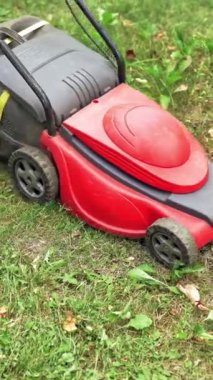 Bahçede çim biçme makinesiyle çalışan bir çocuk. Elektrikli makine bahçede çim kesiyor. Bahçıvanlık açık havada işe yarıyor. Dikey video