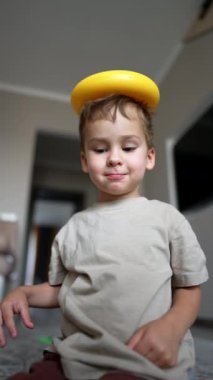 Güzel bebek kafasına piramit bir yüzük taktı. Düşük açı. Çocuk başını eğiyor ve yüzük düşüyor. Dikey video.