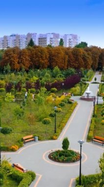 Güzel mimarisi olan şehir parkı. İnsansız hava aracı bahçede uçuyor ve sonra yerleşim bölgesine uçuyor. Dikey video