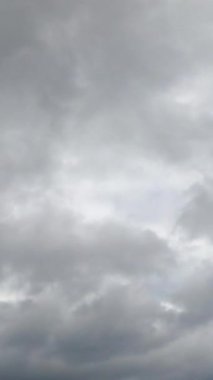Gri bulutların arkasından nadiren mavi gökyüzü görünür. Düşük açılı ufuk çizgisi. Zaman ayarlı. Dikey video