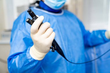 Endoskoplu doktor. Mavi cerrahi kıyafetli bir sağlık çalışanı klinik bir ortamda teşhis prosedürü için bir endoskop hazırlar..