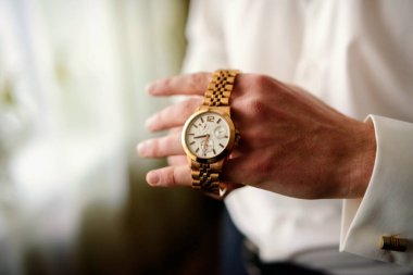 Giyinik bir adamın taktığı zarif bir saat. Resmi kıyafetli bir adam şık ahşap saatini ayarlar, inceliğini ve detaylara olan ilgisini vurgular..