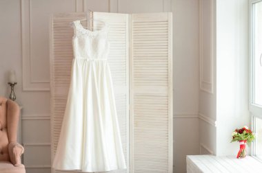 Beyaz elbisenin kapalı mekanı. Göz kamaştırıcı beyaz bir gelinlik, parlak bir odadaki ekranda asılı duruyor. Güzel bir gelinlik ortamı yaratıyor..