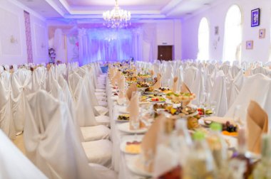 Şık bir salonda şık bir ziyafet. Uzun masalar, beyaz masa örtüleri ve bir dizi lezzetli yemek için güzelce düzenlenmiştir..