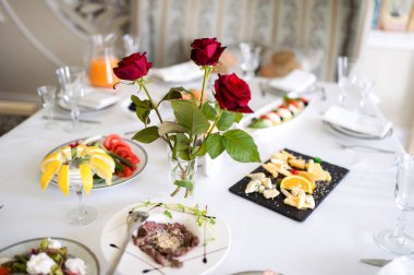 Gül yemeğiyle şık bir yemek. Güzel düzenlenmiş bir masa taze salata, meyve ve peynir tabakları içerir, canlı kırmızı güllerle renklendirilir..