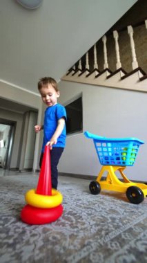 Tatlı bebek, oyuncağın detaylarını el arabasından alır. Tatlı çocuk yere bir piramit inşa ediyor. Düşük açı. Dikey video.