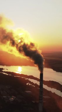 Borular batan güneşe karşı dumanla atmosferi kirletir. Ekoloji kirliliği. Duman yığınları günbatımında göllerin arka planında endüstriden yayılıyor. Dikey video