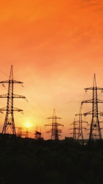 Kırmızı akşam gökyüzüne karşı iletim hatları. Gün batımında yüksek voltajlı elektrik kuleleri. Güzel turuncu günbatımında elektrik direklerinin ve kabloların siluetleri. Hareket kamerası geri. Dikey video