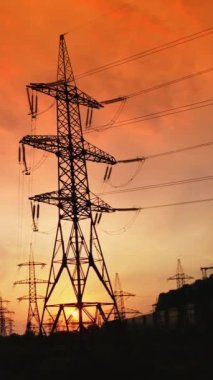 Gün batımında yüksek elektrik kuleleri. Yüksek voltajlı elektrik hattı kablolardan elektrik dağıtır. Akşamları metal direkleri olan dağıtım istasyonu. Ağır çekim. Dikey video