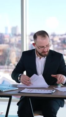 İş yerindeki bir iş adamının portresi. Masada oturan takım elbiseli sakallı bir ofis çalışanı. Dikey video