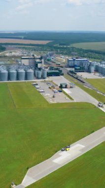 Yeşil doğa arka planında modern bir fabrikanın panoramik görüntüsü. Tahıl asansörleri devrede. Yazın çevre arasında büyük tarım kompleksi. Hava görüntüsü. Dikey video