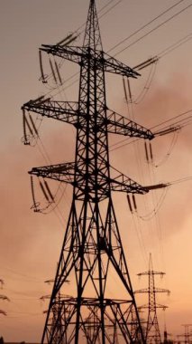 Gün batımında elektrik direkleri. Kirli arka planda yüksek voltajlı elektrik kulesi. Sanayiden gelen zararlı duman atmosferi dolduruyor. Hava kirliliği. Dikey video