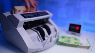 El, nakit sayma makinesine bir yığın turuncu banknot yerleştirir ve çalışmaya başlar. Kadın paraları sayıp masanın üstüne koyuyor. Kapatın. Bulanık arkaplan.