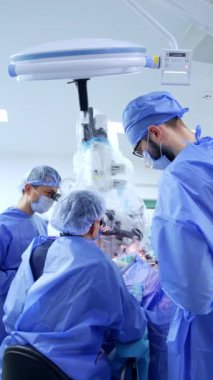 Cerrahın mikroskopta oturup dürbünlere baktığı dikiz görüntüsü. Doktorlara cerrahın her iki tarafında da yardım etmek. Dikey video.