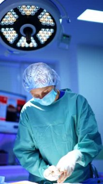 Kadın doktor kesiği dikmek için metal aletler ve iplik kullanıyor. Cerrah ameliyatı bitirir. Dikey video.