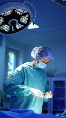 Profesyonel kadın cerrah iğneyi ve ipliği bağlamak için forseps kullanır. Doktor hastayı dikiyor. Dikey video.