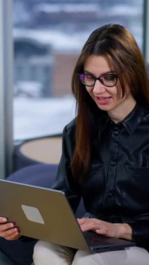 Laptopun klavyesinde yazan gözlüklü esmer kadın. Bayan şaşırdı ya da haber ya da mesajdan heyecanlandı. Arkaplan bulanık. Dikey video