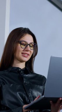 Pozitif kadın elindeki dizüstü bilgisayara bakıyor. Gülümseyen kadın bilgisayarı kapatıyor, gözlüklerini çıkarıyor ve pencereye bakıyor. Düşük açı. Dikey video