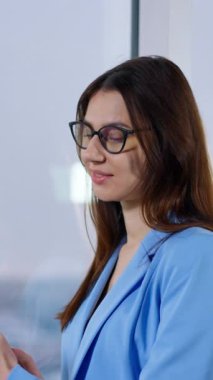 Esmer iş kadını telefonla birini arıyor. Arka plandaki adam pencerede duran dizüstü bilgisayarını kullanıyor. Arka plan bulanık. Dikey video