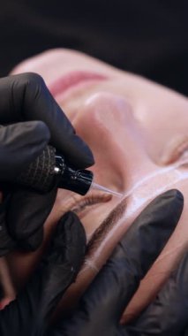 Kalıcı makyaj aleti bir kaş ustasının eldivenli elinde. Kozmetik ve güzellik konsepti. Dikey video