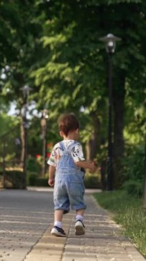 Tatlı çocuk yolun kenarında koşuyor. Çocuk topunu otların arasından alır ve mutlu bir şekilde taşır. Dikey video