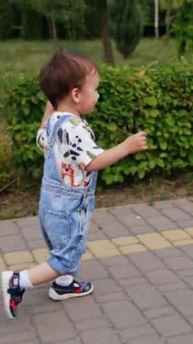 Asfalt yolda koşan beyaz bir çocuk. Aktif çocuk yazın boş zamanlarını parkta geçiriyor. Dikey video