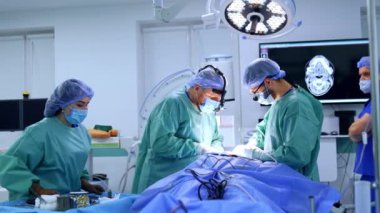 Profesyonel cerrahlar, kadın bir hemşirenin yardımıyla hastayı ameliyat ederler. Erkek anestezi uzmanı arka planda yürür. Tıbbi ekip maksimum yüz ameliyatı yapacak..