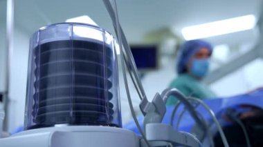 Yapay akciğer ventilatör pompası yavaşça yukarı ve aşağı gider. Ameliyathanede çalışan ekipmanlar. Sağlıkçı bulanık arkaplanda duruyor.
