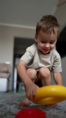 Şirin beyaz çocuk oyuncak piramidin yüzükleriyle neşe içinde oynuyor. Siyah bir kedi kameraya yaklaşır ve bir çocuk. Düşük açı. Dikey video.