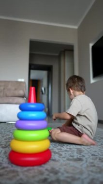 Aktif Kafkas bebek bir piramit inşa ediyor. Sevimli erkek bebek evde neşeyle oynuyor. Dikey video.