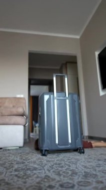 Küçük bebek yerde, büyük gri bir bavulun arkasına saklanıyor. Mutlu gülümseyen neşeli çocuk kameraya yakın dördünün üzerinde emekliyor. Dikey video.