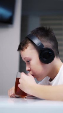 Evde Tablet Kullanan Çocuk. Çocuk tabletine bakarken masada oturup çay içiyor.