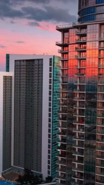 Güneşin batışını yansıtan cam pencereli güzel gökdelenlere yaklaşıyoruz. Miami, Florida, ABD. Arka planda güzel pembe-mavi gökyüzü. Dikey video