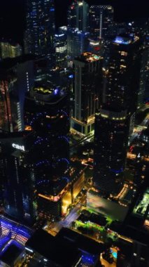 İnsansız hava aracı Miami, Florida, ABD şehir merkezindeki gökdelenlerin üzerine yavaşça iniyor. Şehir ışıkları tepeden. Dikey video