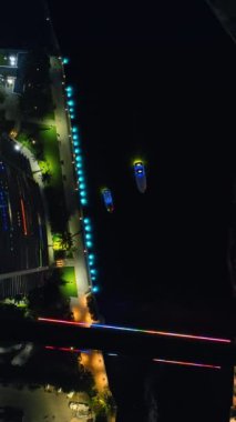 Karanlık nehir boyunca yavaşça giden iki kayık. Gece Miami Nehri 'nin en üst manzarası. Dikey video