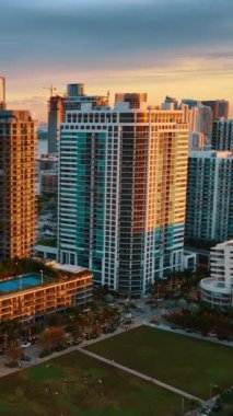Gökdelenlerin ön cephesinde güneşin batışının parlak turuncu ışığı. Gün batımında Miami Beach, Florida, ABD 'de insansız hava aracı görüntüleri yükseliyor. Dikey video