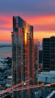 Batan güneşin ışığında Miami Sahili mimarisinin muhteşem manzarası. Şehir merkezindeki modern gökdelenlerin altında sevimli pembe ve mor gökyüzü. Üst Manzara. Dikey video