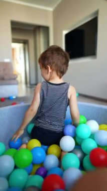 Aktif beyaz çocuk kuru havuzda oynuyordu. Mutlu erkek bebek evde eğleniyor. Dikey video.