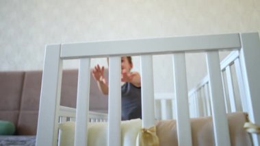 Neşeli küçük çocuk beşiğinde oturuyor. Gülümseyen şirin bebek yatak odasında mutlu mesut oynuyor. Düşük açı görünümü.