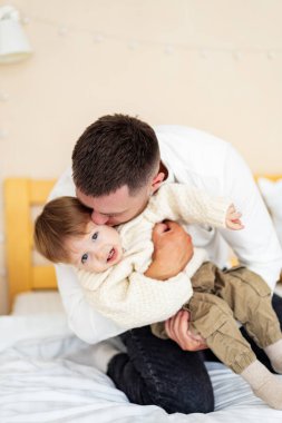 Babam eğlenceyi çocukla paylaşıyor. Bir baba, yürümeye başlayan çocuğuyla neşeli bir anı paylaşır, neşeyle sarılır ve bir yatakta birlikte güler..